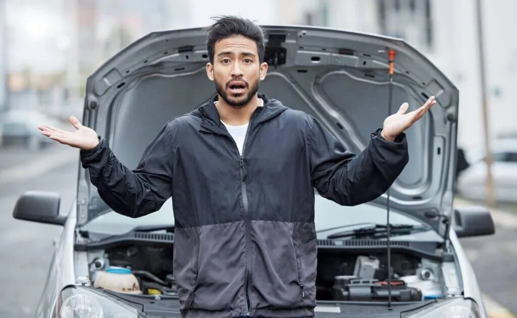 Top 5 Hybrid Car Problems (and How to Avoid Them) 1 Frustrated driver standing in front of a broken-down car with the hood open, shrugging in confusion. The image represents common car issues and the need for reliable auto repair services.