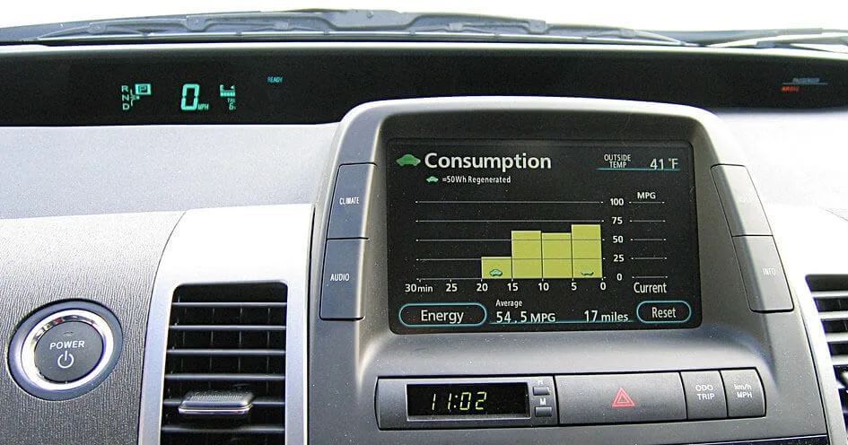 top-5-hybrid-car-problems-suburban-street-epr Close-up of a hybrid car's dashboard showing energy consumption and battery regeneration. The screen displays how much energy is being saved while driving, with a graph tracking fuel efficiency and battery recharge. The dashboard also includes a digital speedometer, gear indicators, and a power button, highlighting the car’s eco-friendly hybrid system.