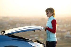 Young woman opening the hood of a broken hybrid car – hybrid battery issues – Newark NJ auto repair