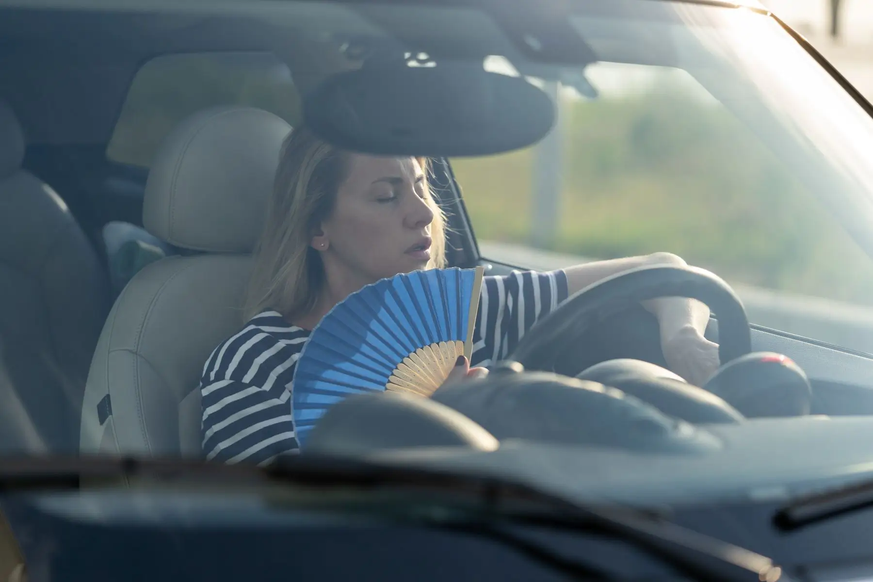 Frustrated woman fanning herself inside a hot car with broken AC