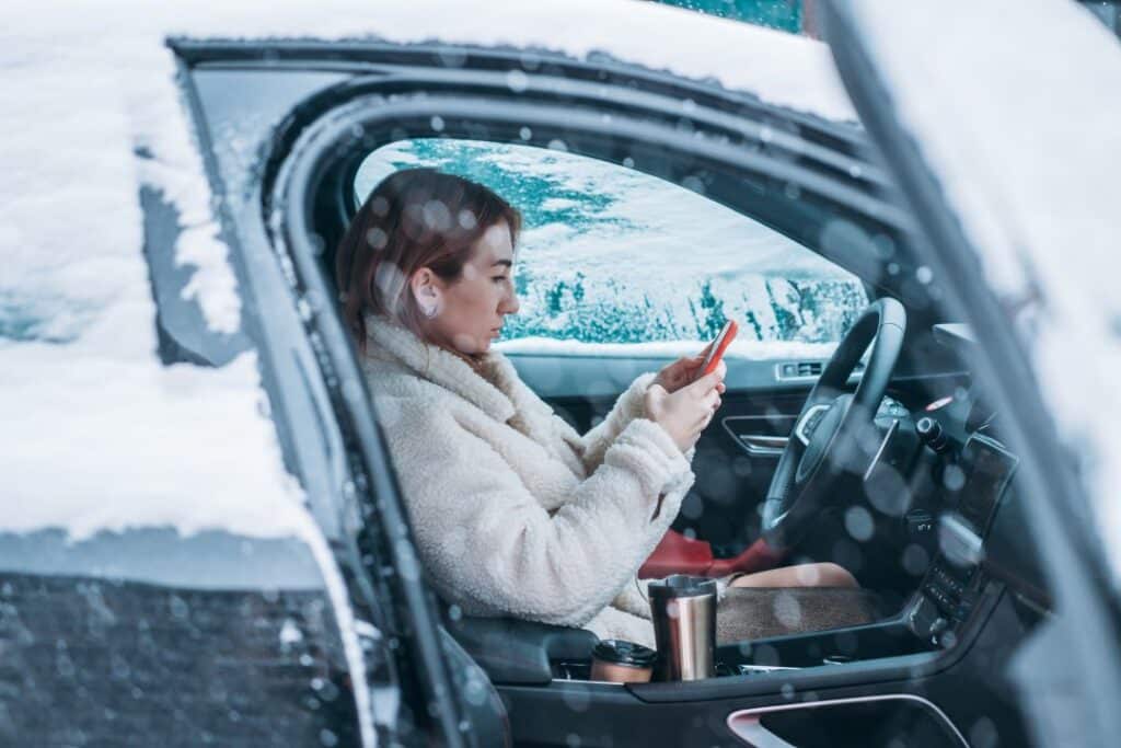 Woman driver checking phone inside car during winter — cooling system protection and car maintenance in Newark NJ