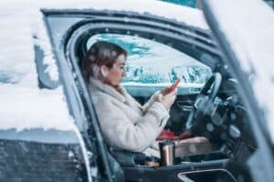 Woman driver checking phone inside car during winter — cooling system protection and car maintenance in Newark NJ