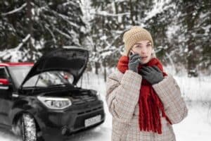 Woman standing by her car in winter, talking on the phone after a cold morning start — symbolizing the importance of winter car maintenance in Newark, NJ.